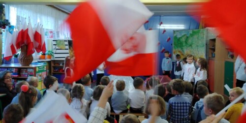 dzieci machają państwowymi flagami w tle trwa występ