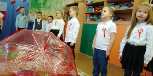 parasole biały i czerwony leży na dywanie za nimi dzieci śpiewają piosenki