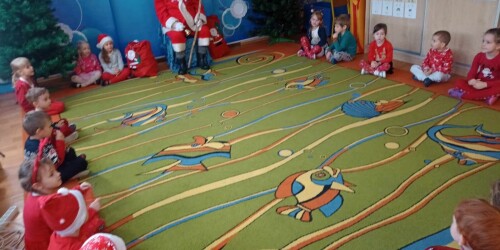 Dzieci siedzą w kole na dywanie z Mikołajem