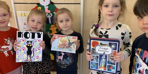 cztery dziewczynki prezentują nagrody jakie otrzymały dzieci: gra, puzzle, książeczki