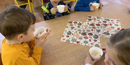 piątka dzieci siedzących przy stoliku pije czekoladą z kubeczków
