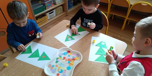 dzieci ozdabiają kółkami choinkę z papierowych trójkątów