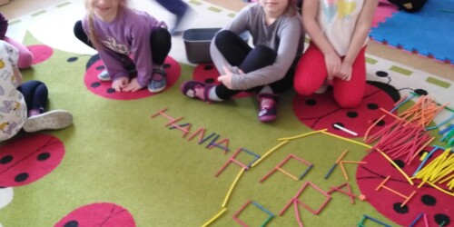 Dzieci układają literki z patyczków na dywanie