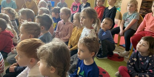 dzieci siedzą na dywanie i słuchają z zaciekawieniem
