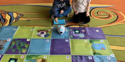 chłopiec z dziewczynka siedzący przy macie i programujący robota edukacyjnego