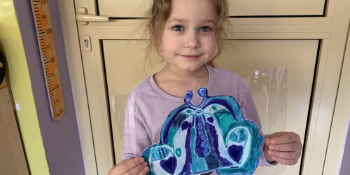 dziewczynka ubrana na fioletowo prezentuje pracę plastyczna przedstawiającą niebiego motyla
