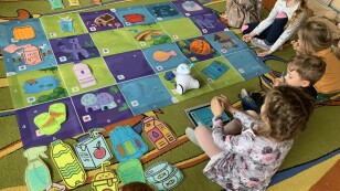 dzieci siedząc na dywanie projektują na tablecie trasę robota