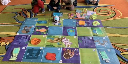 dzieci siedząc na dywanie projektują na tablecie tracę robota
